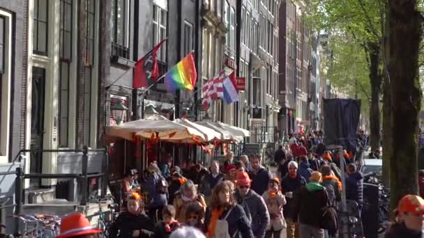 纽西兰 Amsterdam 2019年4月27日 阿姆斯特丹市国旗 彩虹同性恋旗和荷兰国徽 人们走在旧城区的街道上庆祝国王节 — 图库视频影像