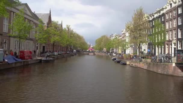 オランダのアムステルダム 27エイプリル社 2019 アムステルダム市内中心部の運河をまたぐアムステルダム川の船と橋 オランダに美しい古いオランダの家 — ストック動画