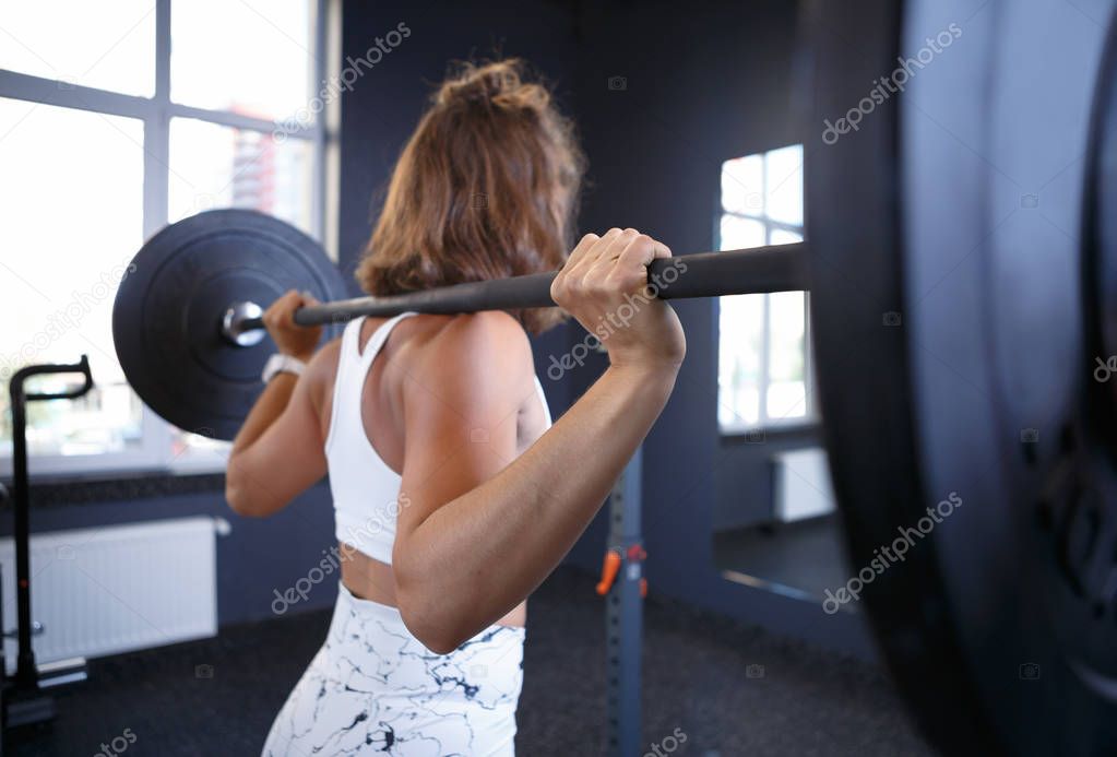 Young female athlete doung squats with heavy weight barbells in gym