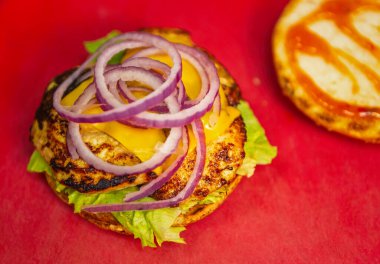 Fast food restoranının mutfağında doğal malzemeli tavuk burger pişirmek. Tavada taze et filetosu, çedar peyniri dilimi, marul salatası ve kırmızı soğan halkaları ile ızgara yapılmış hamburger.