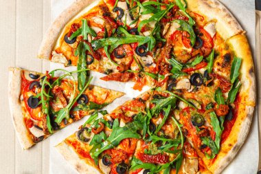 Lezzetli İtalyan üst görüntüsü. Fast food karton kutuda servis ediliyor. İnce hamurda fırında pişirilen lezzetli doğal malzemeler. Siyah zeytin, roka yaprağı, kurutulmuş domates, beyaz şampiyon mantarlar.