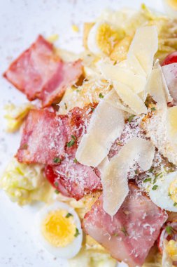 Restoranda doğrudan yukarıdan çekilen gurme sezar salatası. Doğal malzemeli lezzetli İtalyan atıştırmalıkları: parmesan peyniri, pastırma eti şeritleri, bıldırcın yumurtası ve beyaz tabakta marul.