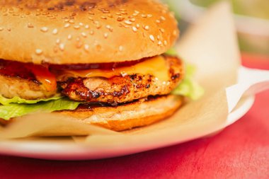 Amerikan fast food restoranında kahverengi kağıt ve beyaz tabakta servis edilen tavuk çizburgeri. Marul salatası, peynirli ve kabuklu çörekle pişirilmiş lezzetli kümes hayvanları köftesi. 