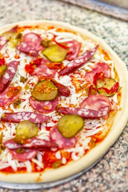 Pişirmek için çiğ pizza. Fast food restoranı menüleri almak için İtalyan restoranında fırında pişirmeye hazır. Pizzacı, sosisli, salatalıklı, peynirli, domates soslu lezzetli doğal yiyecekler pişiriyor.