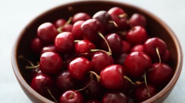 Lezzetli kırmızı kiraz meyvelerinin kahverengi seramik kasede beyaz mermer masa üzerinde görüntüsü. Yazın kahvaltıda sunulan lezzetli doğal tatlı yemekleri videosu. Tabakta lezzetli tatlı kirazlar.