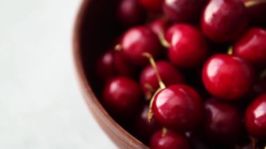 Lezzetli kırmızı kiraz meyvelerinin kahverengi seramik kasede beyaz mermer masa üzerinde görüntüsü. Yazın kahvaltıda sunulan lezzetli doğal tatlı yemekleri videosu. Tabakta lezzetli tatlı kirazlar.