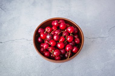 Kahverengi seramik kasede olgun kırmızı ekşi kirazlar gri mermer arka planda servis edilir. Yaz mevsiminde kahvaltı için lezzetli doğal tatlı.
