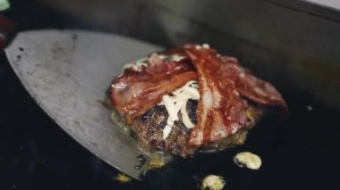 Pastırma şeritli hamburgerler pişir. Fast food restoranı şefi sıcak ızgara tavada pişir. Profesyonel mutfak işçisi spatula aletli çizburger pişiriyor.