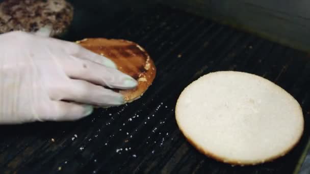 夕食のためのファーストフードレストランでグリルパンに揚げゴマと2つのハンバーガーのパン 近い映像でハンバーガーを調理 ビデオで調理されている伝統的なアメリカのダイナーカフェの食事 — ストック動画