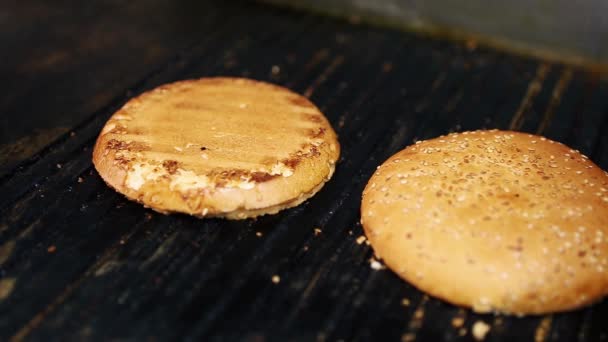 烤面包 用芝麻做的面包 放在烤架上 与脚靠得很近 在快餐店的厨房里 用新鲜的粗硬的面包做汉堡包 在火热的表面烤着吃晚餐 — 图库视频影像