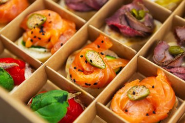 Yemek servisi için karton kutuda lezzetli aperatifler. Kırmızı balık fileto, kapari ve şarap partisi için egzotik deniz ürünleri atıştırmalıkları.