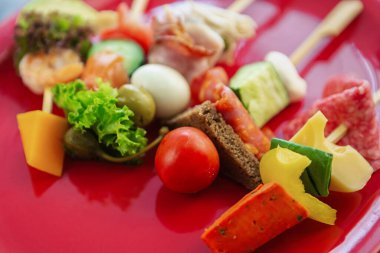 Kırmızı tabakta servis edilen çubuklarda taze atıştırmalıklar. Ahşap çubukta gurme atıştırmalıklar. Şarap partisi aperatifleri için sağlıklı ve doğal malzemeler.