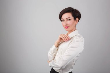 Stüdyoda poz veren kendinden emin genç bir iş kadını. 30 'lu yaşlarda güzel beyaz bir kadın model. Resmi beyaz tişört giyiyor, klasik kırmızı ruj ve kısa saç kesimi.