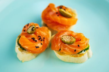 Ekmeğin üzerinde kırmızı balık bulunan antipasti atıştırmalıkları mavi seramik tabakta sunuluyor. Şarap partisi için lezzetli atıştırmalıklar. Akdeniz restoranında deniz mahsulleri olan kanepe.