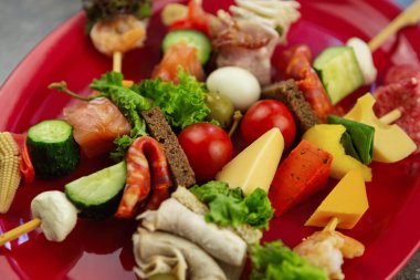 Kırmızı seramik tabakta servis edilen şarap partisi atıştırmalıkları. Alami sosisi, kiraz domatesleri, paprika peyniri, somon balığı, öğle yemeği için hazırlanmış dana eti.