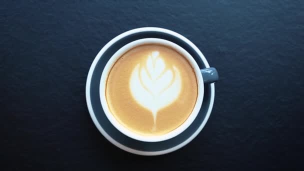 Kupa friss reggeli cappuccino kávé kerámia bögre filmezett közvetlenül felülről.Videóklip forró energetikai ital reggelire.Élvezze aromás olasz latte virágos rajz hab réteg