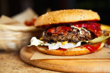 Pastırmalı Amerikan hamburgeri ızgarada pişirildi, fast food retaurantında ahşap tabakta servis edildi. Domuz çizgili lezzetli burger, biftek köftesi, ketçap sosu, susamlı marul salatası.