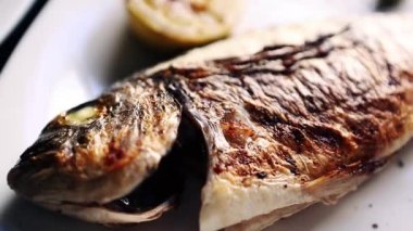 Izgarada bütün deniz levreği balığı, deniz ürünleri restoranında beyaz seramik tabakta servis edilir. Akşam yemeği için ızgarada pişmiş lezzetli kızarmış deniz kabuğu. Asya lokantasında pişirilmiş Suzuki balığının video klibi.