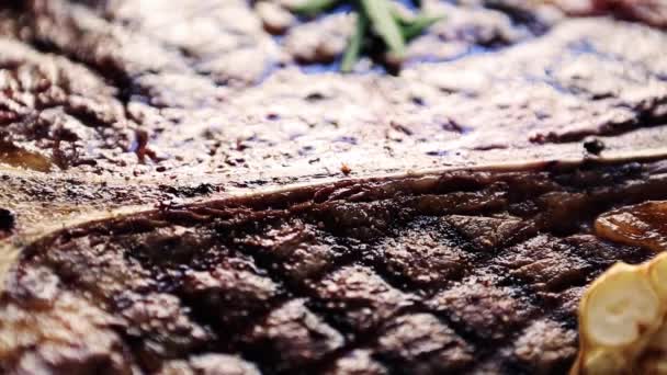 肉料理店の白いプレートで提供される焼きTボーンステーキは ズームアウト効果で上から撮影されました ピーマンで焼き上げられた牛肉片のビデオクリップ ダイナーカフェでの夕食のためのローズマリースパイス — ストック動画