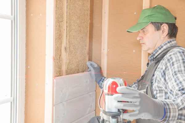 Stellt der Arbeiter die Nachbearbeitungsarbeiten der Wände mit dem weißen Holzbrett her, die Ebene der Laserlinie verwendend. Gebäude wärmeisolierendes Öko-Holzrahmenhaus mit Holzfaserplatten — Stockfoto