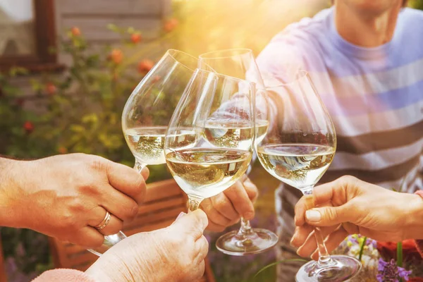 Family of different ages people cheerfully celebrate outdoors with glasses of white wine, proclaim toast People having dinner in a home garden in summer sunlight. Stock Picture