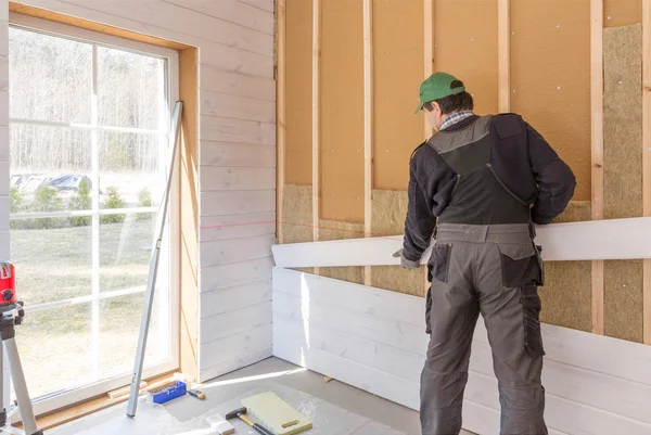Pracownika sprawia, że prace wykończeniowe na ściany z biały deska, za pomocą lasera liniowe. Budynku ciepło izolacyjne płyty z włókien drzewnych eco drewniana rama domu — Zdjęcie stockowe