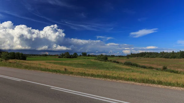 Road bergop met groen grasveld onder witte wolken en blauwe hemel. — Stockfoto