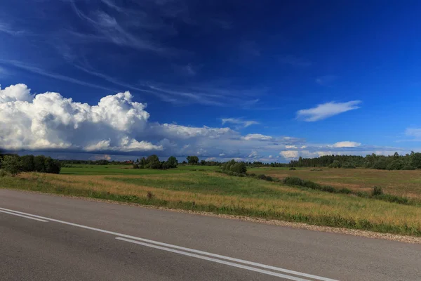 Road bergop met groen grasveld onder witte wolken en blauwe hemel. — Stockfoto