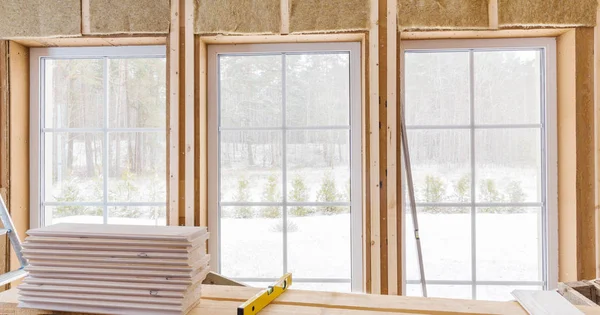 Wärmeisolierendes Öko-Holzrahmenhaus mit Holzfaserplatten und wärmeisolierendem natürlichen Hanfmaterial. Fertigung der Wände und eines großen Fensters mit einer weißen Holzplatte mittels Laserlinienwaage — Stockfoto