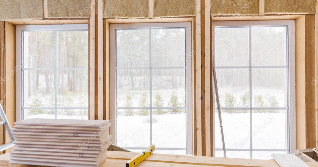 Thermally insulating eco-wood frame house with wood fiber plates and heat-isolating natural hemp material. Finishing the walls and a large window with a white wooden board, using laser line level