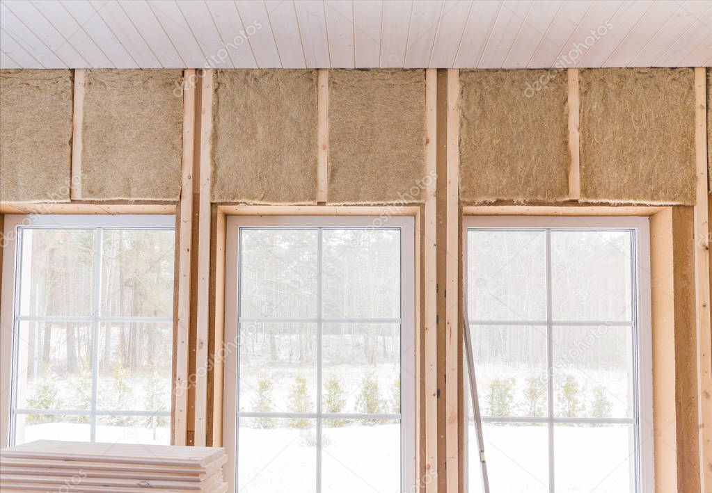 Thermally insulating eco-wood frame house with wood fiber plates and heat-isolating natural hemp material. Finishing the walls and a large window with a white wooden board, using laser line level