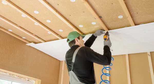 Ο εργαζόμενος κάνει τελειώματος του τοίχους με λευκή ξύλινη σανίδα, χρήση του λέιζερ επίπεδο γραμμής. Κτίριο μόνωσης θερμότητας eco-ξύλινο πλαίσιο σπίτι με πλάκες ξύλινων ινών Φωτογραφία Αρχείου
