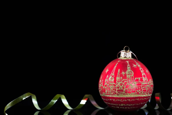 Boule de Noël rouge avec une peinture dorée de la vieille ville et un ruban d'or sur fond noir . — Photo