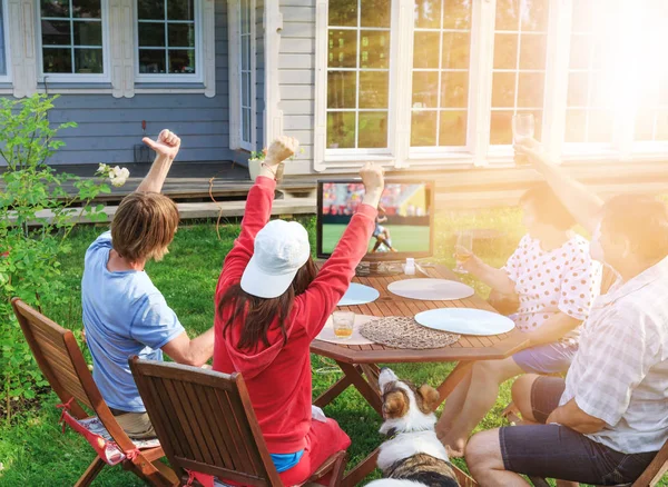 Счастливая семья или компания друзей смотрят футбол по телевизору во дворе своего дома . — стоковое фото