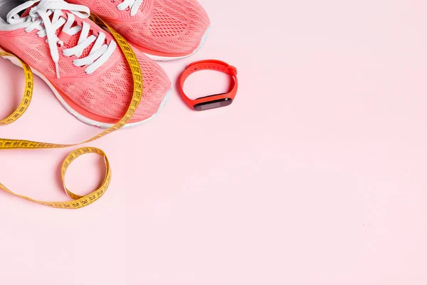 Fittnes sport composition with pink sneakers, smart bracelet, measuring tape on pink background.