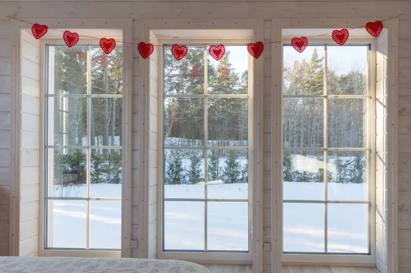 Велике біле вікно спальні в дерев'яному будинку прикрашене романтичною гірляндою червоних сердець на день Святого Валентина. — стокове фото
