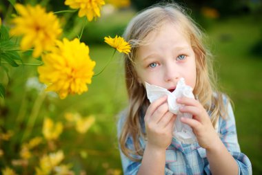 Cute little girl blowing her nose by beautiful yellow coneflowers on summer day. Allergy and asthma issues in small kids. Healthy living. clipart