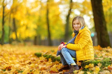 Sevimli küçük kız güzel sonbahar gününde eğleniyor. Sonbahar parkta oynayan mutlu çocuk. Sarı sonbahar yaprakları toplama çocuk. Çocuklar için sonbahar faaliyetleri.