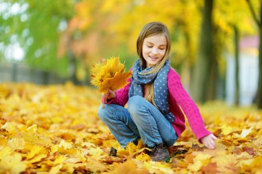 Sevimli küçük kız güzel sonbahar gününde eğleniyor. Sonbahar parkta oynayan mutlu çocuk. Sarı sonbahar yaprakları toplama çocuk. Çocuklar için sonbahar faaliyetleri.