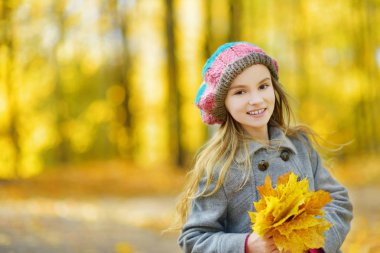 Sevimli küçük kız güzel sonbahar gününde eğleniyor. Sonbahar parkta oynayan mutlu çocuk. Sarı sonbahar yaprakları toplama çocuk. Çocuklar için sonbahar faaliyetleri.