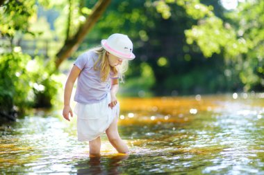 Sevimli küçük kız sıcak yaz gününde bir nehir kenarında oynuyor. Çok güzel çocuk açık havada yaz tatil sırasında eğleniyor. Çocuklar için su aktiviteleri.