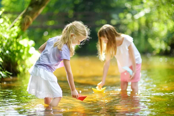 遊んで二つの妹は暖かく 日当たりの良い夏の日に川でのボートを紙します 水で楽しい様子 小さな子供のための夏の活動 — ストック写真