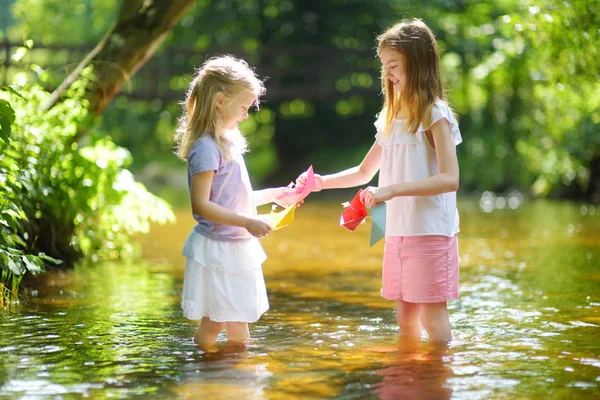 两个小妹妹在温暖晴朗的夏日里在河边玩纸船 孩子们在水里玩得很开心 幼儿暑期活动 — 图库照片