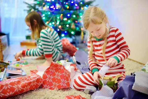 愛らしい妹のギフトを開くとアンラップ クリスマスの朝プレゼント クリスマス パジャマを着てします 家庭でクリスマスを祝う — ストック写真