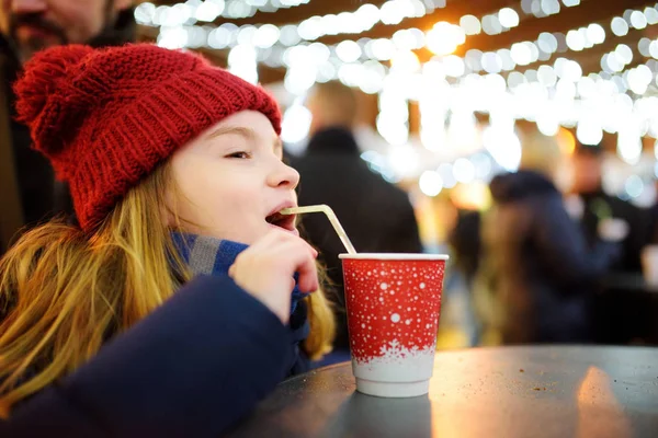 伝統的なクリスマス マーケットでホット チョコレートを飲むかわいい女の子 魔法のクリスマスの時期にお菓子 キャンディー ジンジャーブレッドを楽しむ子供 — ストック写真