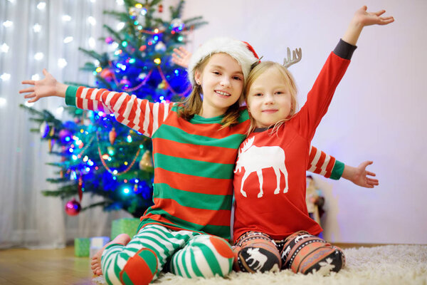 Two adorable sisters decorating a Christmas tree with colorful glass baubles at home. Family leisure at wonderful Xmas time. Trimming a festive tree.