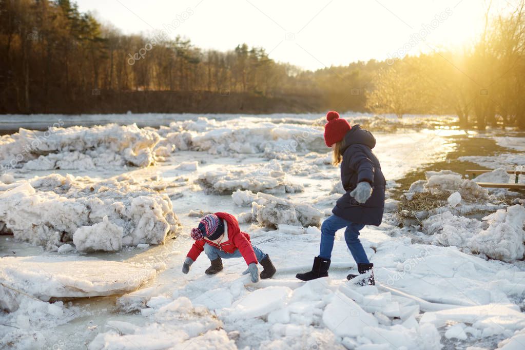 Two happy sisters playing with ice blocks by frozen river during an ice break. Children having fun in winter. Winter activities for kids.