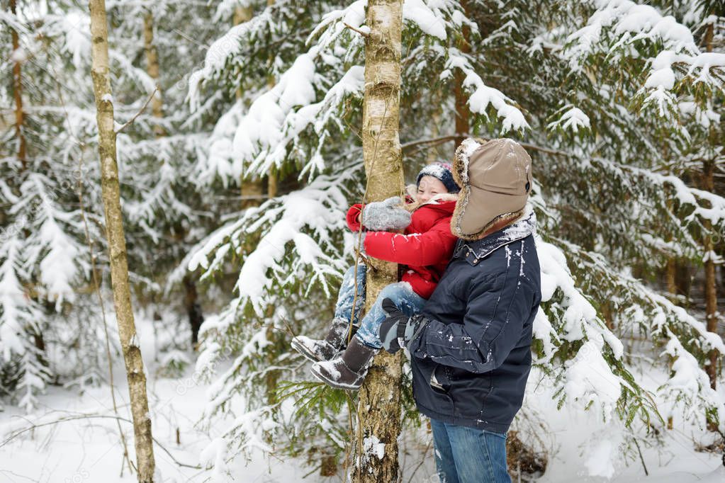 Adorable little girl and her grandpa having fun in beautiful winter forest. Happy child playing in a snow. Winter activities for kids.