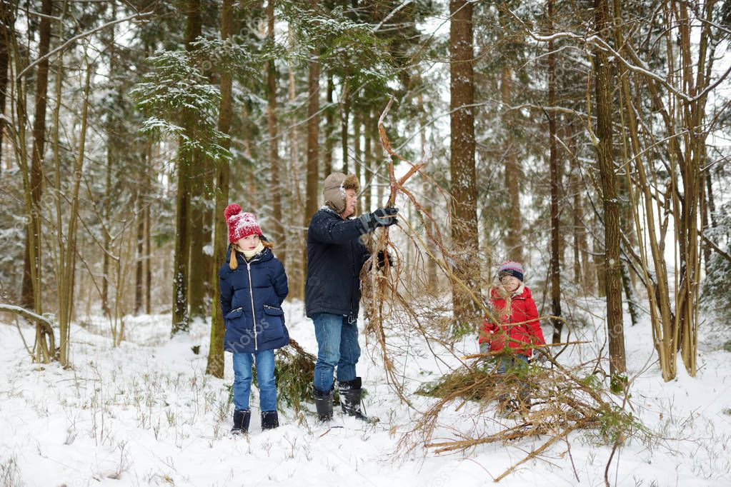 Adorable little girls and their grandpa having fun in beautiful winter forest. Happy children playing in a snow. Winter activities for kids.