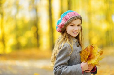 Sevimli küçük kız güzel sonbahar gününde eğleniyor. Sonbahar parkta oynayan mutlu çocuk. Sarı sonbahar yaprakları toplama çocuk. Çocuklar için sonbahar faaliyetleri.